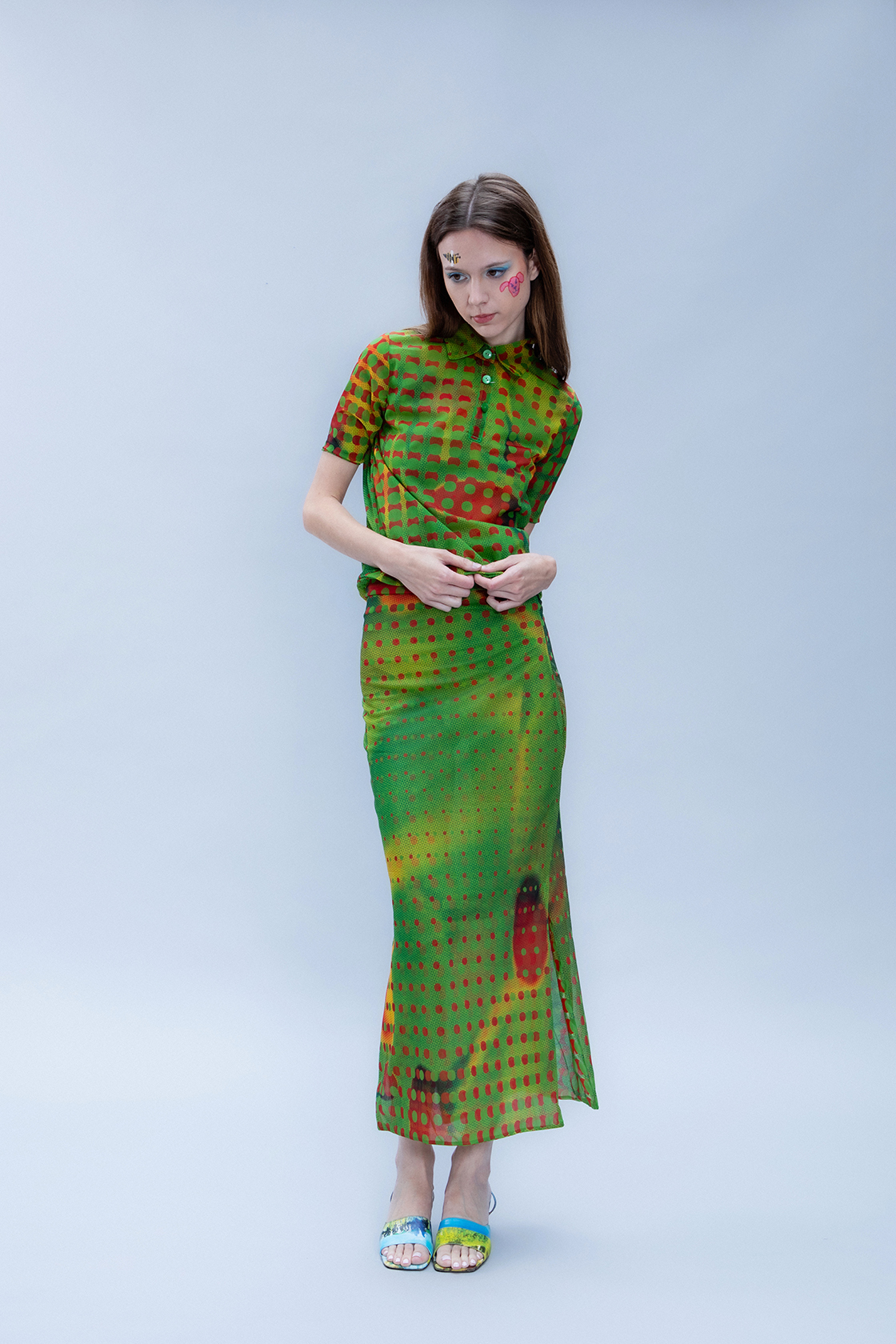 Full body shot of a model with hands on her hips in a green patterned dress agaist a gray backdrop